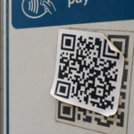 Layered QR code sticker on a public payment sign showing how QR codes can be tampered with for AI scams.