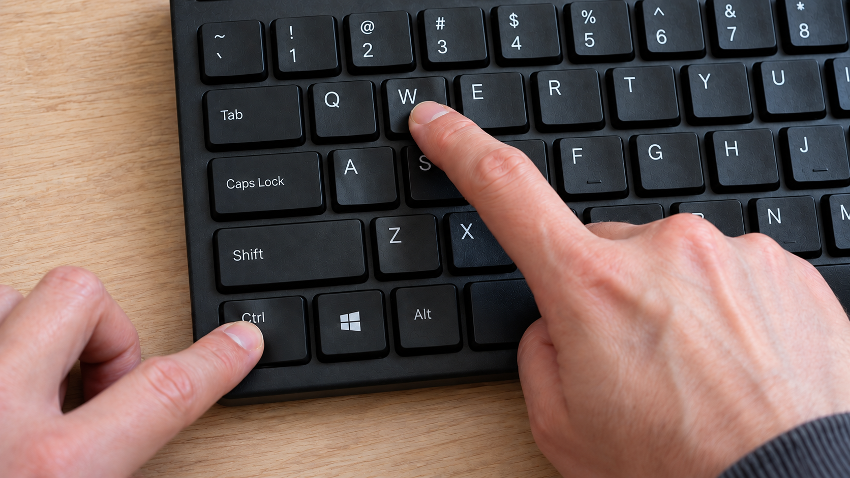 Two hands press the Ctrl and W keys on a computer keyboard.