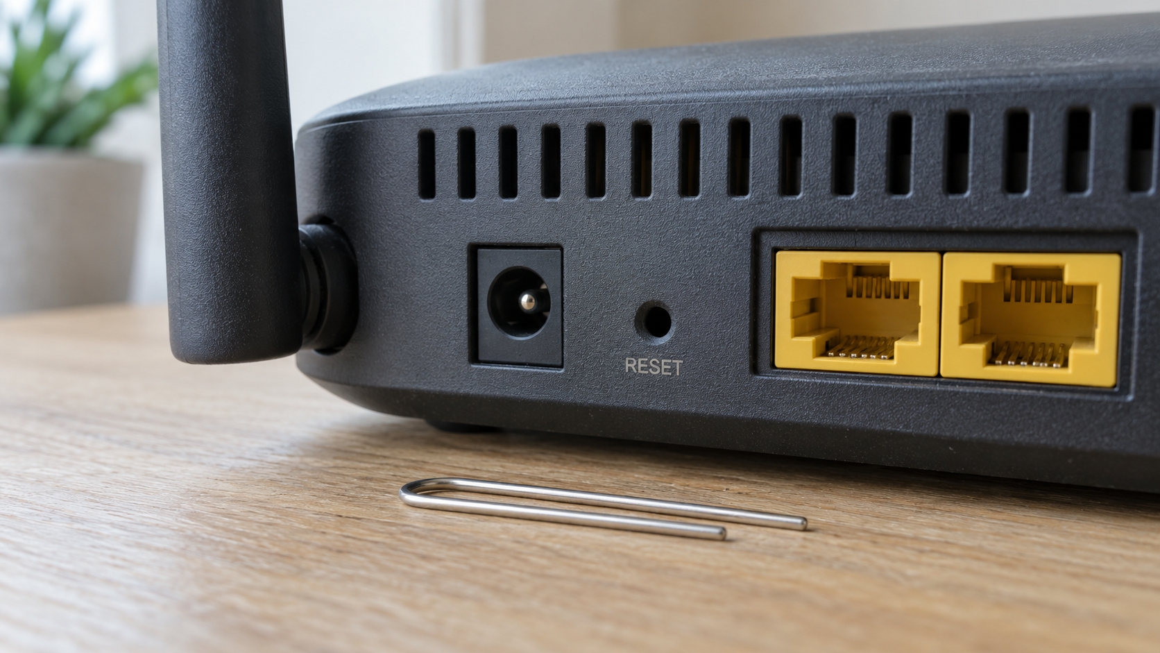 Recessed RESET pinhole on a router beside an unused straightened paperclip.